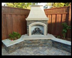 an outdoor fireplace in the middle of a brick patio with a wooden fence behind it