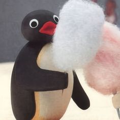 a toy penguin holding a fluffy ball of yarn