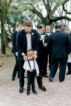 a young boy in a tuxedo is being held by his father at a wedding