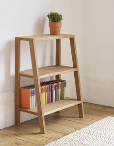 a wooden shelf with books on it next to a white rug and a potted plant