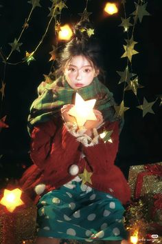 a young woman holding a lit candle in her hands while sitting on a pile of presents