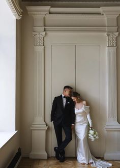 a bride and groom standing next to each other in front of a wall with columns