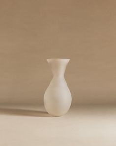 a white vase sitting on top of a table next to a brown wall and floor