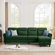 a green couch sitting in front of a window next to a rug on top of a wooden floor