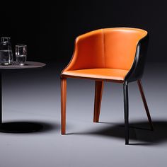 an orange and black chair next to a small table with glasses on it, in front of a dark background