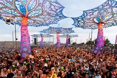 a large group of people standing in front of colorful structures at an outdoor music festival