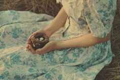 a woman sitting on the ground holding a bird's nest with her hands in it