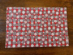 a red and white checkered cloth with snowflakes on it, sitting on a wooden table