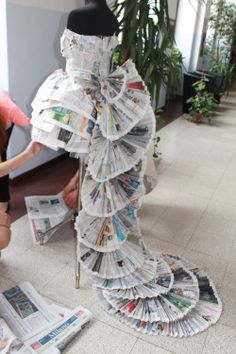 a woman kneeling down next to a mannequin made out of newspapers