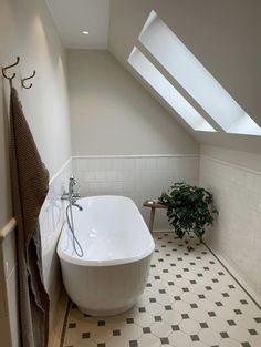 a white bath tub sitting under a window next to a plant in a room with black and white tile flooring