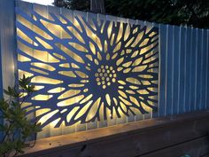 a decorative metal screen on the side of a wooden fence with lights shining through it