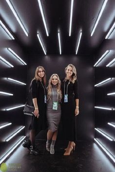 three women standing in front of a black wall with neon lights on the walls and floor