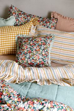 a bed covered in lots of pillows and blankets with colorful flowers on the pillow cases