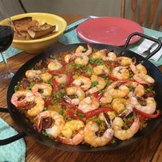 a pan filled with shrimp and vegetables on top of a table next to a glass of wine