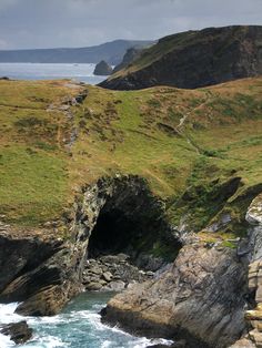 an ocean view with some rocks and water in the foreground, and green hills on the far side