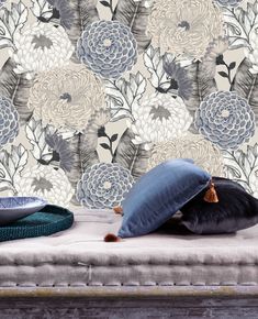 a blue pillow sitting on top of a bed next to a wallpapered background