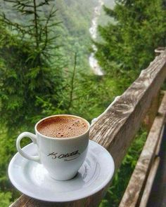 a cup of coffee sitting on top of a saucer next to a wooden railing