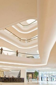 people are standing on the escalators in a large building with white walls and ceilings