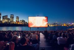 people are sitting in chairs watching a movie on the big screen at dusk by the water