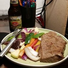 a white plate topped with meat and veggies next to a bottle of beer