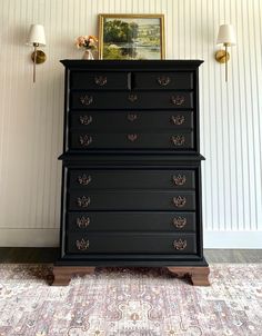 a black dresser sitting in front of a painting on the wall