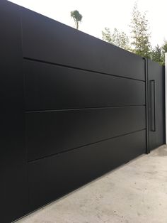 a large black gate is next to a white fence