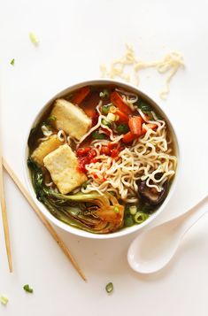 a bowl of noodles, tofu and vegetables with chopsticks on the side