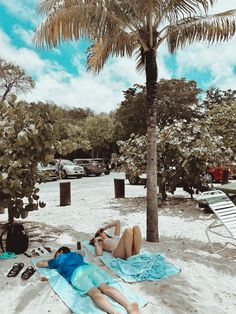 two people laying in the sand under a palm tree on a beach with blue towels and flip flops