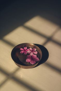 a bowl with flowers in it sitting on a table next to a shadow cast wall