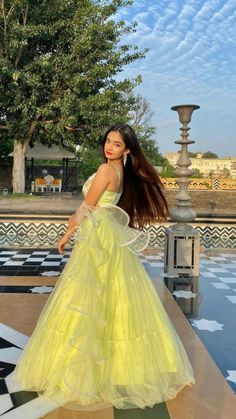 a woman in a yellow dress is standing near a fountain and looking at the camera