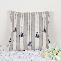 a black and white striped pillow with tassels on it next to some flowers