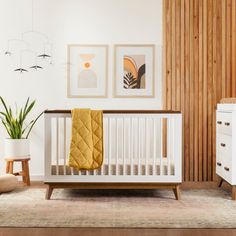 a white crib with a yellow blanket on it in front of wooden paneled walls