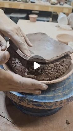 a person is making something out of clay on top of a blue bowl and another person is using a knife to cut it