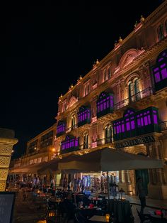 an illuminated building at night with tables and chairs in the foreground, lit up by purple lights