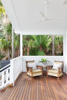 two chairs sitting on top of a wooden floor next to a white porch with palm trees