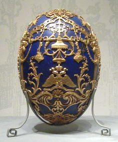 an ornately decorated blue and gold egg on a metal stand in front of a wall