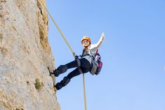 a man climbing up the side of a mountain with his hands in the air while holding on to ropes