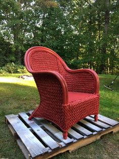 a red wicker chair sitting on top of a wooden pallet in the grass