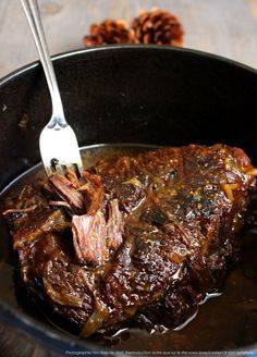 a piece of meat is being cooked in a skillet with a fork and some pine cones