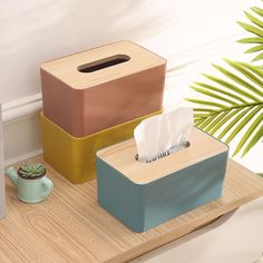 three tissue dispensers sitting on top of a wooden table next to a plant