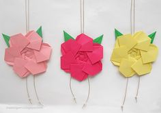 three different colored paper flowers are hanging from strings on the wall, one is pink, one is yellow