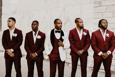 a group of men standing next to each other wearing red suits and bow ties with their hands in their pockets