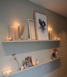 candles and pictures are displayed on the wall above a shelf in a room with wood flooring