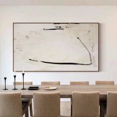 a dining room table with beige chairs and a large painting on the wall above it