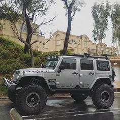 a silver jeep parked in front of a building on a rainy day with trees and buildings behind it