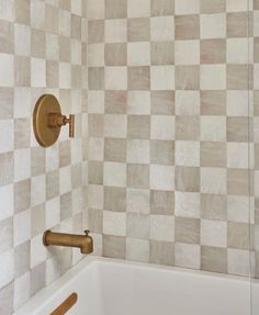 a bath tub sitting next to a tiled wall with gold fixtures on the faucet