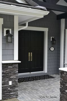 a black front door on a gray house with white trim and brick walkway leading up to it