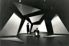 two men sitting on the floor in front of large black and white geometric shapes,