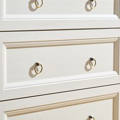 a white dresser with gold handles and two rings on the drawer knobs in front of it