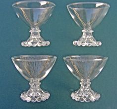 four clear glass goblets sitting side by side on a blue surface, one is empty